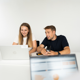 PRIMAS Eine Frau und ein Mann schauen auf einen Laptop, im Vordergrund ist ein Laptop mit PRIMAS geöffnet