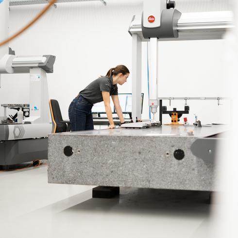 Eine Frau lehnt sich an eine KMG und beobachtet die Vermessung eines Bauteils